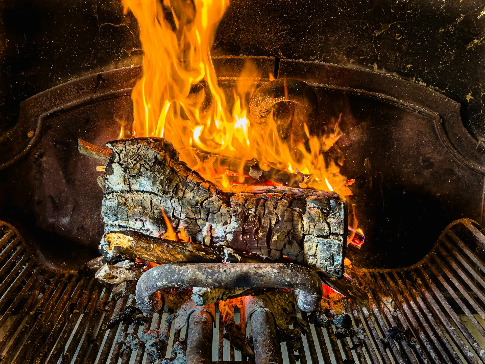 Troncos de encina ardiendo en una parrilla, con llamas tras la reja