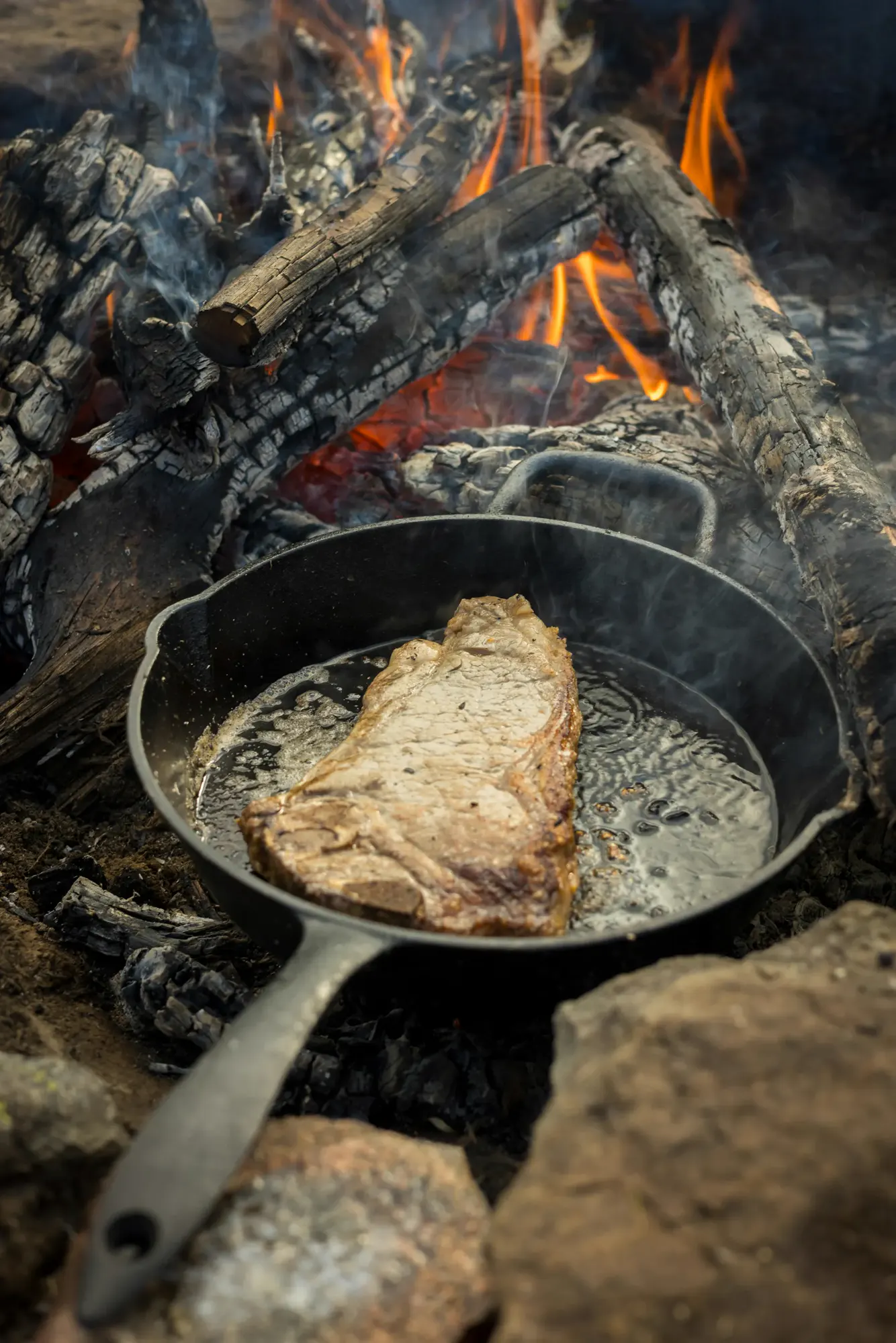 Un chuletón grueso sellándose en una sartén de hierro sobre brasas